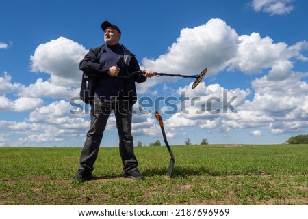 Man with metal detector. Man on field with sensor to search for metal. Treasure hunter stands on background blue sky. Treasure hunter holds modern metal detector. Guy with shovel looking for treasure
