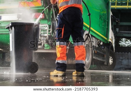 Caucasian Garbage Truck Operator Pressure Washing Black Trash Can After Waste Collection. Junk Truck Built In Washer Using. Royalty-Free Stock Photo #2187705393