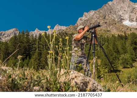 Traveling Nature Photographer Standing in the Middle of Scenic Landscape Taking a Photo of the Alpine Mountains With His Camera Mounted on a Tripod.