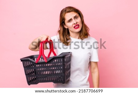 young pretty woman  feeling puzzled and confused. empty shopping basket concept