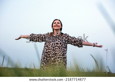 beautiful woman in her fifties standing outdoors in a field spreading her arms
