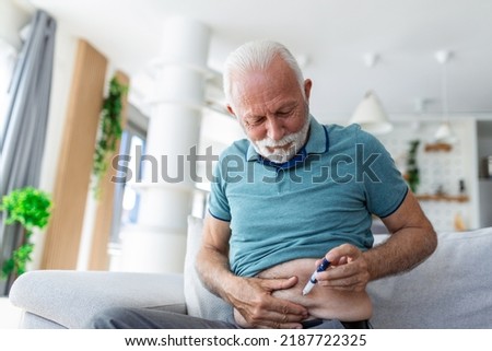 Senior man sitting on sofa and giving himself an insulin injection for his diabetes Royalty-Free Stock Photo #2187722325