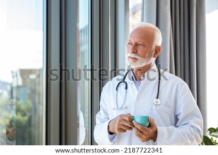 Portrait of senior mature health care professional, doctor, with stethoscope holding blue cup of coffee,