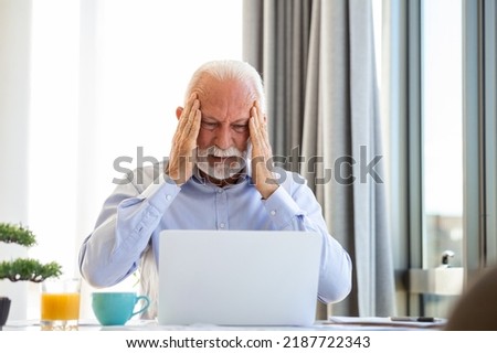 Stressed mature businessman with laptop. He could also have a headache. He is sitting in the boardroom. There are documents and laptop on the table. Copy space