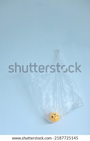 A hanging transparent plastic bag with sadness emoticon. Global warming concept. Plastic pollution ecology problem.