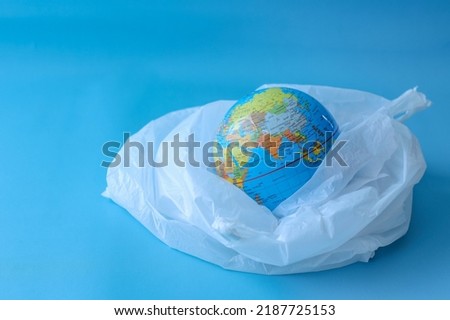 A globe in a plastic bag on blue background. The concept of protecting the world from plastic waste and environmental pollution.