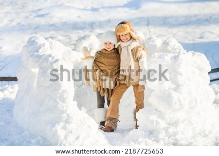Happy family have fun playing in snow fort on sunny winter day. Smiling children pose looking at the camera. Beautiful winter vacation.