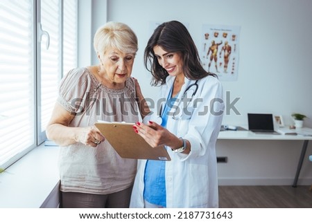 Doctor and patient are discussing. Focused two different generations doctors looking at clipboard, discussing patient's illnesses or diagnosis in clinic. Young nurse assisting older female patient