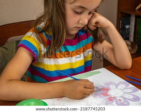 Close-up of a girl drawing with colored paints on paper.