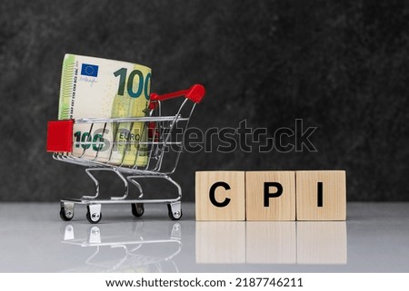 Cash money rolls in shopping trolley, euro banknotes whith wooden blocks with word CPI on white table on dark grey background. CPI, consumer price index symbol Royalty-Free Stock Photo #2187746211