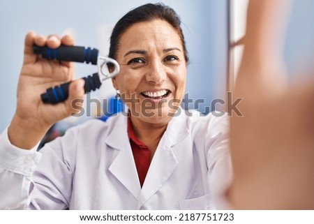 Middle age hispanic woman physiotherapist making selfie by the camera at rehab clinic