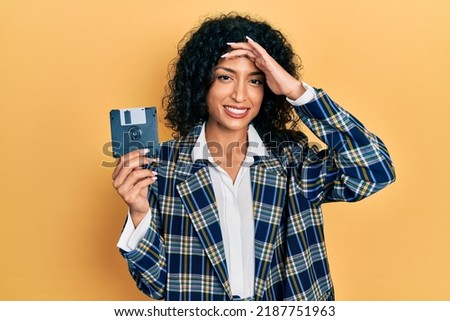 Young latin girl holding floppy disk stressed and frustrated with hand on head, surprised and angry face 