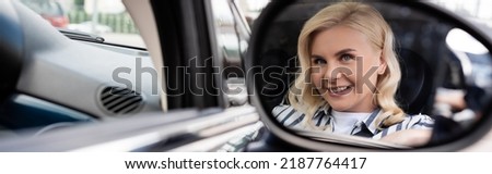 Cheerful blonde woman reflecting in blurred mirror of auto, banner