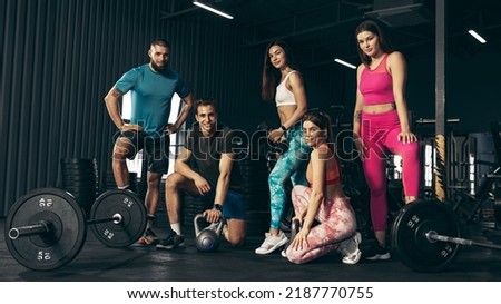 Group of young friends doing sports, training, posing at gym indoors. Maitaining healthy and sportive lifestyle. Concept of health, sportive lifestyle, fitness, beauty, body care, diet