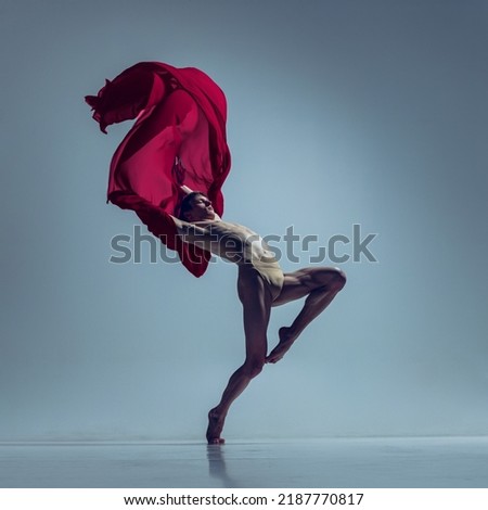 Inner world. Portrait of young man, flexible ballet dancer in action with red fabric, cloth isolated on navy studio background. Grace, art, beauty, contemp dance concept. Weightless, flexible actress