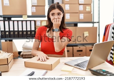 Young hispanic woman preparing order working at storehouse looking stressed and nervous with hands on mouth biting nails. anxiety problem. 