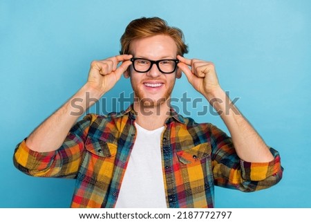 Photo of smart handsome stylish guy with red hairstyle dressed checkered shirt arms spectacles smiling isolated on blue color background