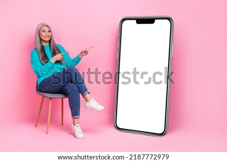 Photo of beautiful lady pensioner dressed blue pullover sitting chair pointing device empty space isolated pink color background