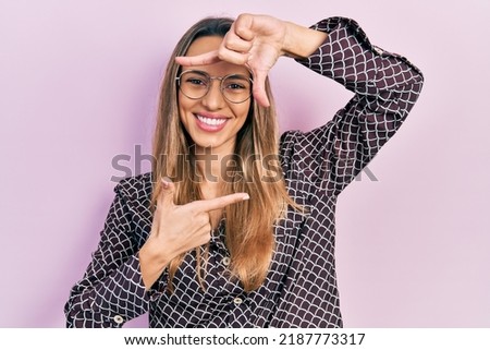 Beautiful hispanic woman wearing casual clothes and glasses smiling making frame with hands and fingers with happy face. creativity and photography concept. 