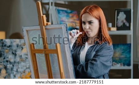 Portrait pensive red-haired Caucasian woman paints in room thinking about idea create picture ponder think drawing hobby talented girl painting on canvas with acrylic contemporary art work in studio