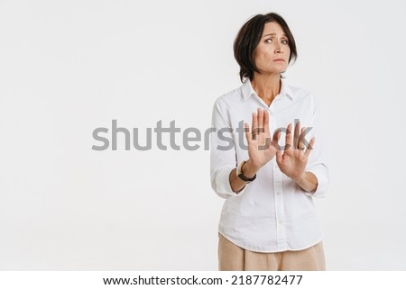 Mature brunette woman frowning while making stop gesture isolated over white background