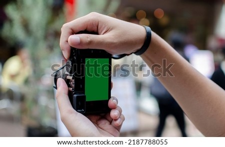 Two man hand man holding mirroless camera with green screen in bokeh blurred crowd of people and shops