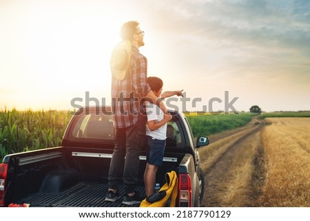 father and son standing on trunk of truck on farmland Royalty-Free Stock Photo #2187790129