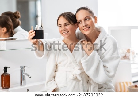beauty, hygiene, morning and people concept - happy smiling mother and daughter taking selfie with smartphone at bathroom