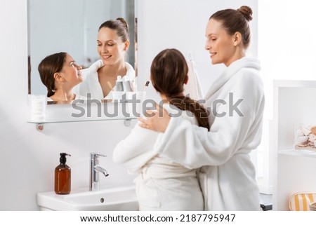 beauty, hygiene, morning and people concept - happy smiling mother and daughter in front of mirror at bathroom