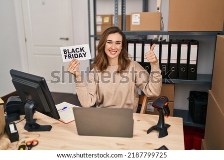 Young beautiful woman holding black friday banner small commerce smiling happy and positive, thumb up doing excellent and approval sign 