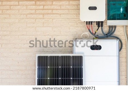 Front view of photovoltaic panel and battery instalation leaning on the beige white wall with no people renewable energy Royalty-Free Stock Photo #2187800971