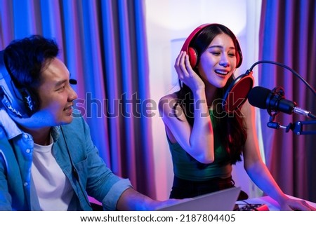 Asian audio DJ man and woman speaks into microphone to broadcasting. Young beautiful female and male blogger influencer wearing headphones and recording morning news podcast show for radio at studio.
