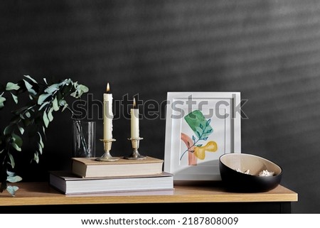 interior and home decor concept - bench with burning candles, picture in frame, books, seashells and eucalyptus branches over black background