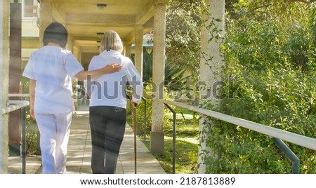 Asian doctor helping elderly retired woman with walker stick in the hospital yard. Rehabilitation concept. Royalty-Free Stock Photo #2187813889