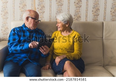 Happy caucasian senior couple using a new smartphone, smiling to each other and discussing text messages while sitting on a sofa in the living room. High quality photo