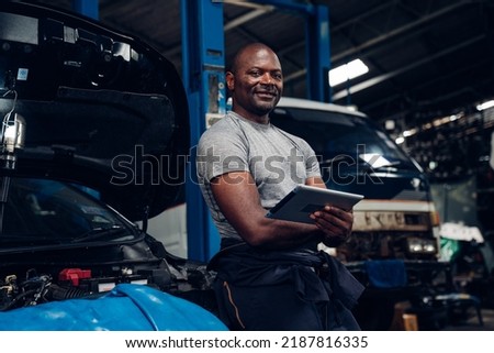 Portrait of an auto mechanic holding tablet at the repair garage. Repair service.