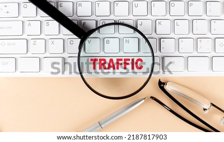 Text TRAFFIC on a keyboard with magnifier , glasses and pen on beige background