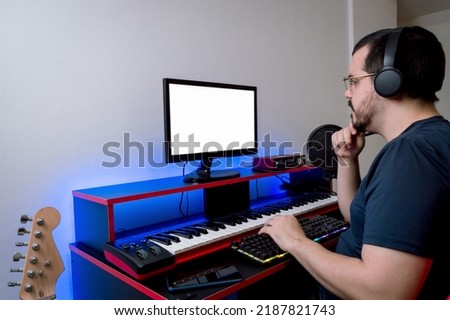 caucasian latin man with headphones and glasses, working sitting in his home music studio thinking with a hand on his chin looking at the monitor, music industry concept with copy space.