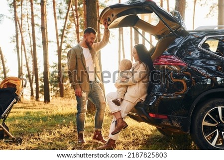 With black colored automobile. Happy family of father, mother and little daughter is in the forest. Royalty-Free Stock Photo #2187825803