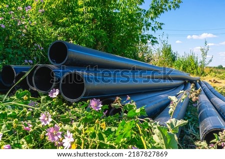 Large diameter plastic pipes for outdoor water supply. HDPE pipes lie in the field. Smooth black plastic pipes with a blue stripe on a grass background. Laying of water supply systems.
