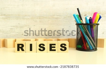 Five stacked wooden cubes with letters RISES on a white desktop on a gray background. Business concept