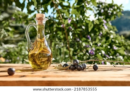 Extra virgin olive oil and olive branch in the bottle on wooden table in the olive grove. Healthy mediterranean food. Royalty-Free Stock Photo #2187853555