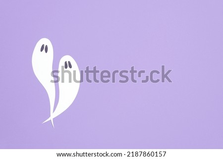 Cute minimal halloween composition, couple of white ghosts flying on lilac background, pastel color design with copy space.