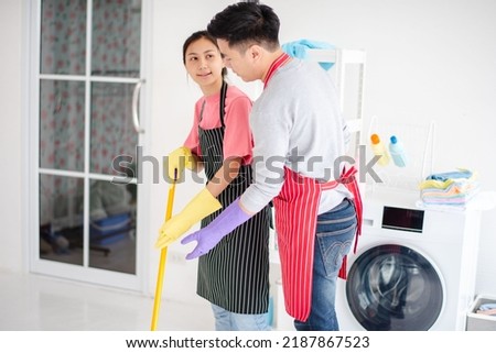 Couples help clean the house, wife is mopping the floor, next to a bucket to change the water and mop the floor. Husbands are competing to mop the floor. It's a romantic picture feel like in a movie.