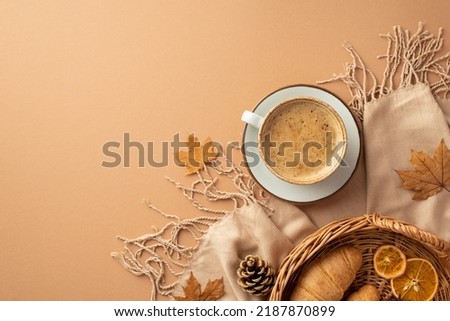 Autumn aesthetic concept. Top view photo of cup of hot drinking on saucer wicker tray with croissants dried orange slices autumn maple leaves scarf and pine cones on isolated beige background Royalty-Free Stock Photo #2187870899
