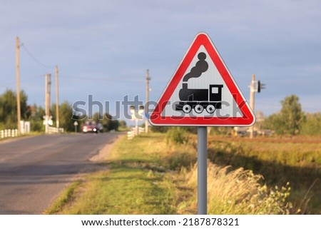 Railway road sign in red and white, railway crossing sign, in the background a car is moving over the rails