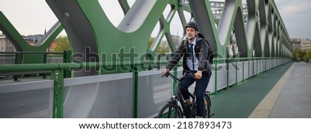 Businessman commuter on the way to work, riding bike over bridge, sustainable lifestyle concept. Wide shot. Royalty-Free Stock Photo #2187893473
