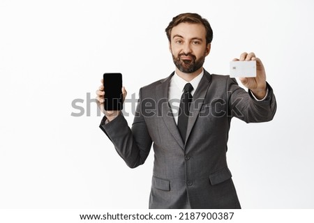 Skeptical businessman showing his credit card, smartphone screen, mobile phone interface, dislike something, standing over white background