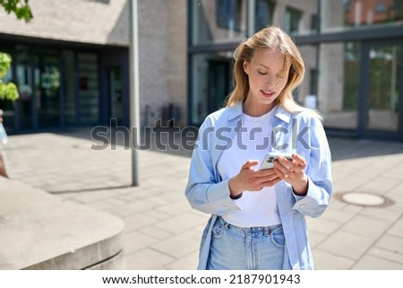 Girl university student user holding cell phone using mobile applications tech on smartphone looking at cellphone, chatting, texting, checking social media, educational apps standing outside campus.