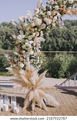 A wedding arch decorated with a composition of fresh flowers for an outdoor wedding ceremony. Fashionable wedding decor. Royalty-Free Stock Photo #2187922787